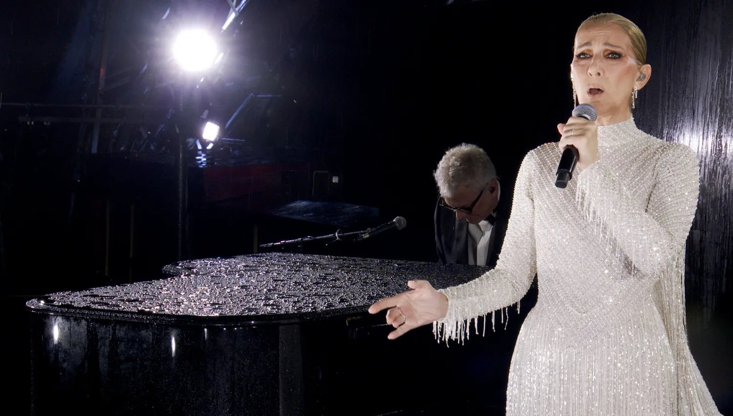 Celine Dion in a white sequined dress singing at the Olympics