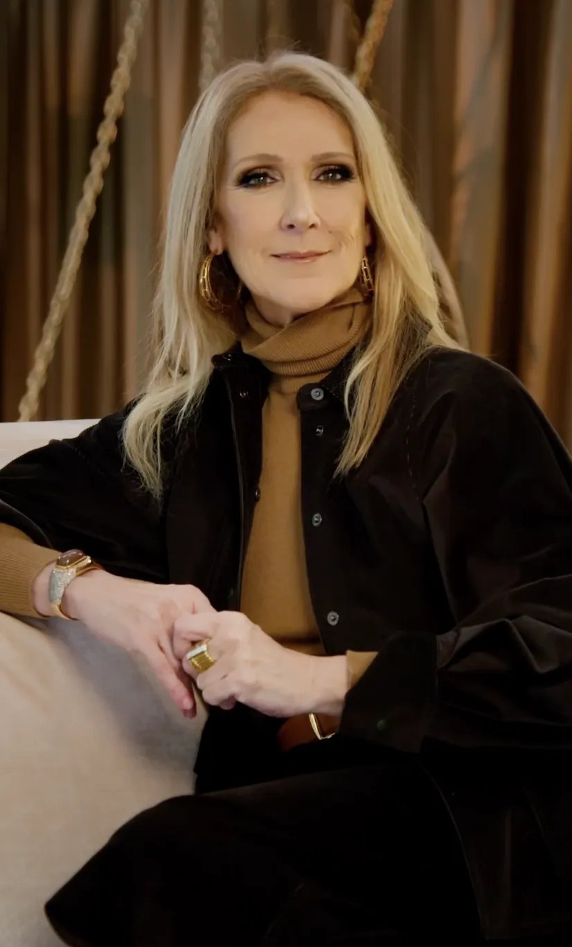 Celine Dion in a brown jacket, brown turtleneck, brown pants, brown boots, and hoops, sitting on a sofa