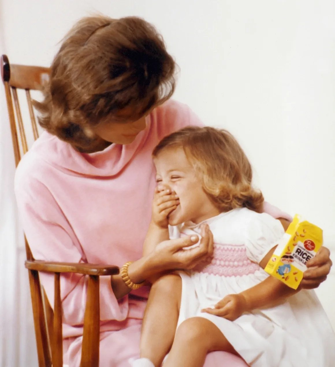 Jacqueline Kennedy (née Bouvier, 1929 - 1994) as she holds her daughter Caroline as the latter eats cereal, Hyannis Port, Massachusetts, Spring or Summer 1959.