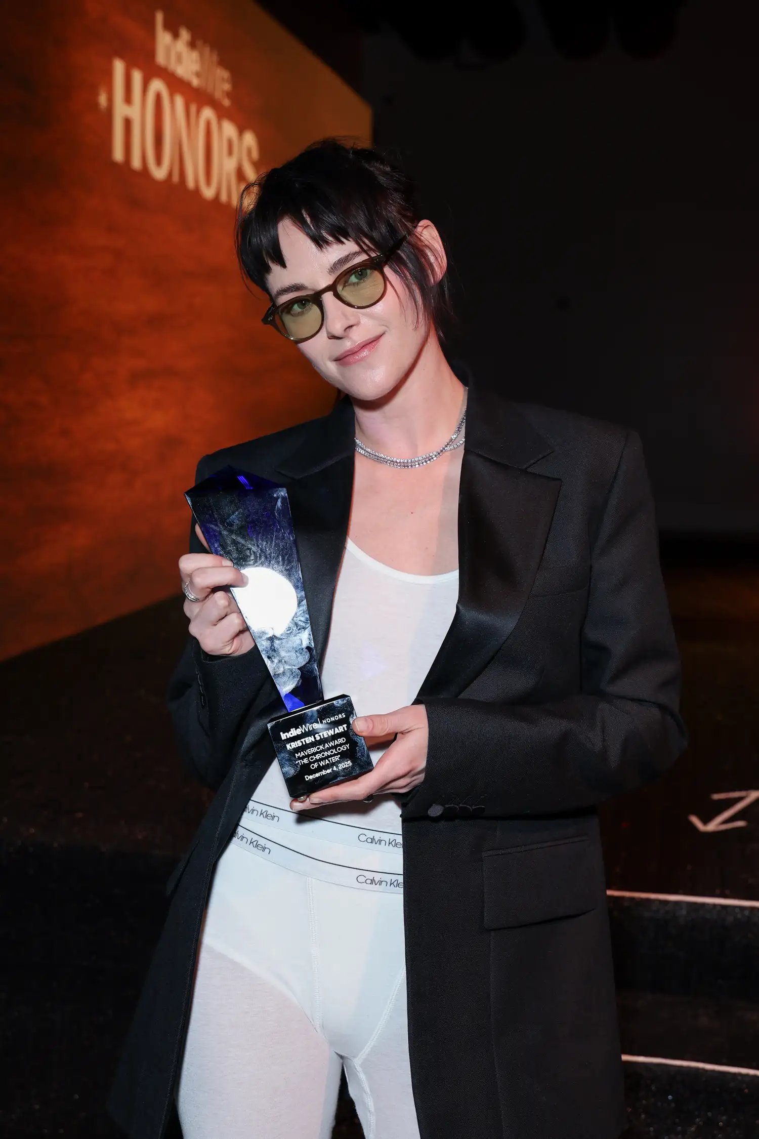 Kristen Stewart in sheer white Calvin Klein underwear with a black blazer on the red carpet with an award