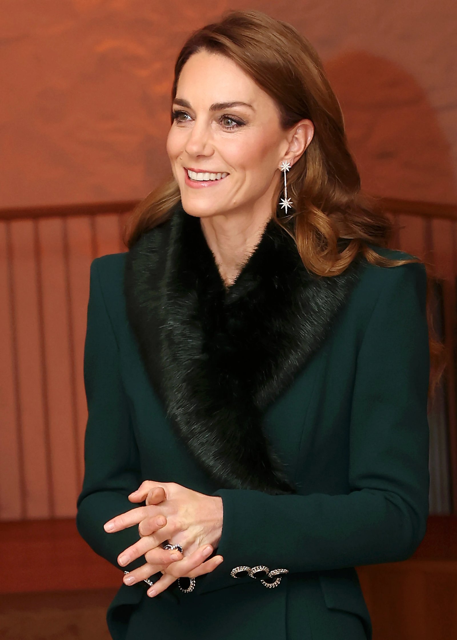 Catherine, Princess of Wales, smiles, looking left, with her hands clasped.