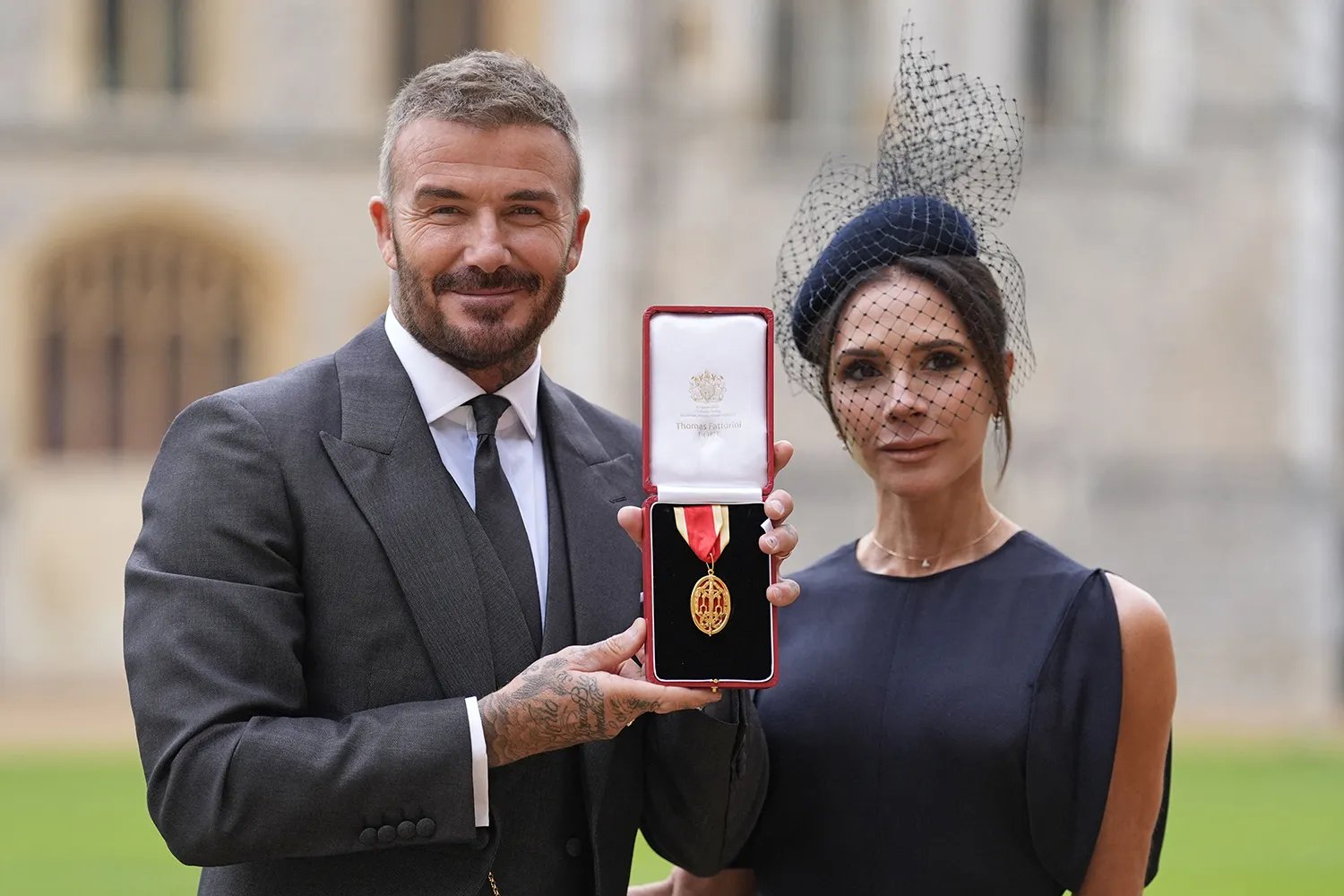 Former England footballer David Beckham (L) poses next to his wife singer and fashion designer Victoria Beckham (R) with his medal after being appointed as a Knight Bachelor (Knighthood) for services to sport and charity