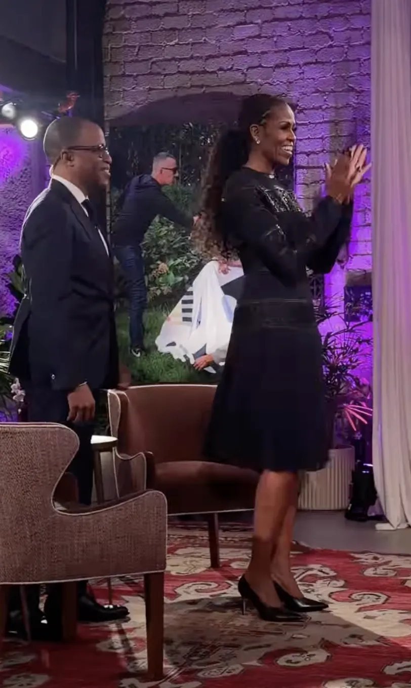 Michelle Obama in a black striped dress with a pleated skirt and a long ponytail