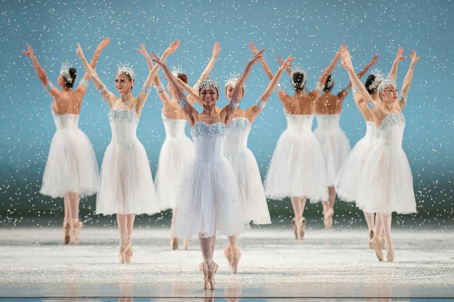 Ballet dancers on stage performing in coordinated poses under falling snow effects