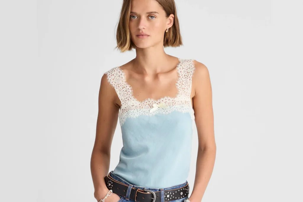 Woman in a light blue lace-trimmed camisole with jeans and a studded belt.