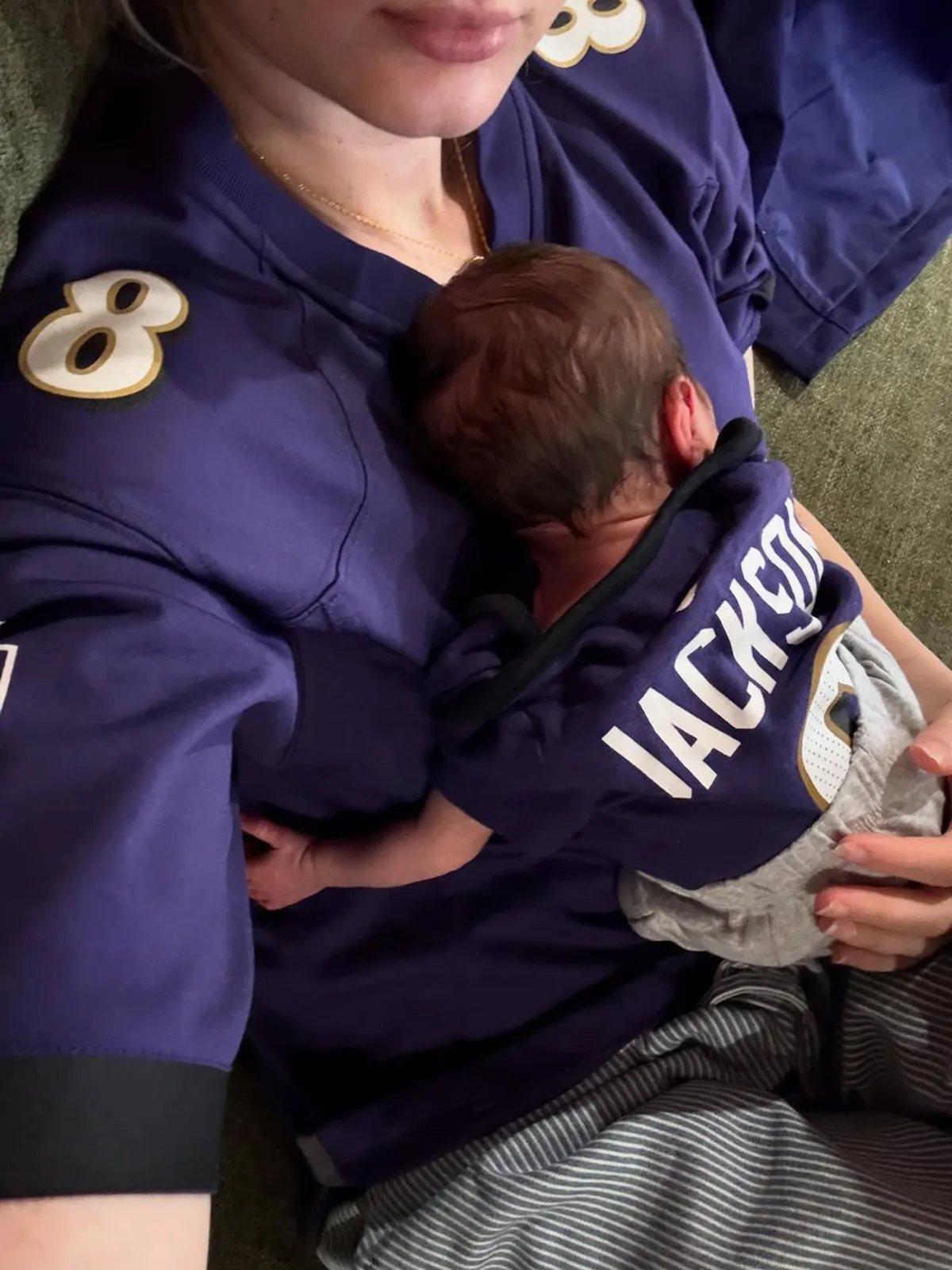 A person wearing a sports jersey holds a baby dressed in a small matching jersey with the name Jackson printed on it both reclining