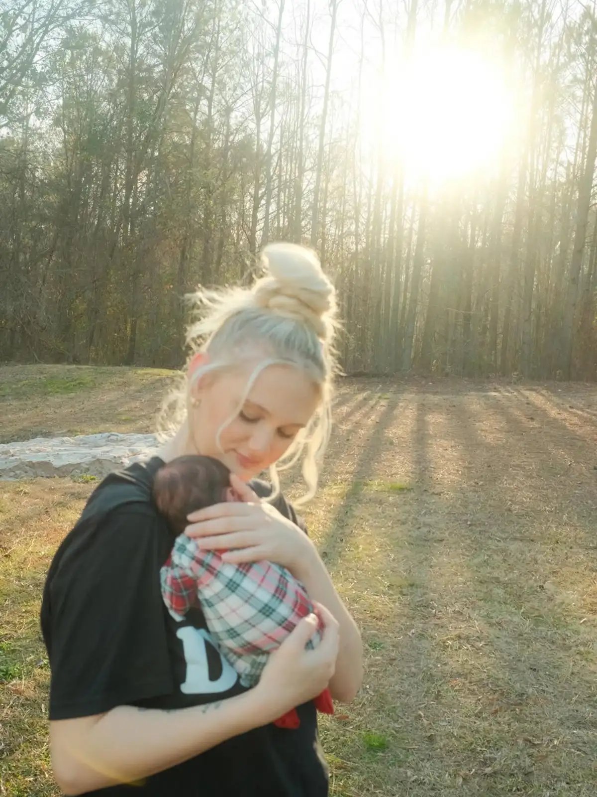 A woman cradling a baby outdoors in a sunlit garden