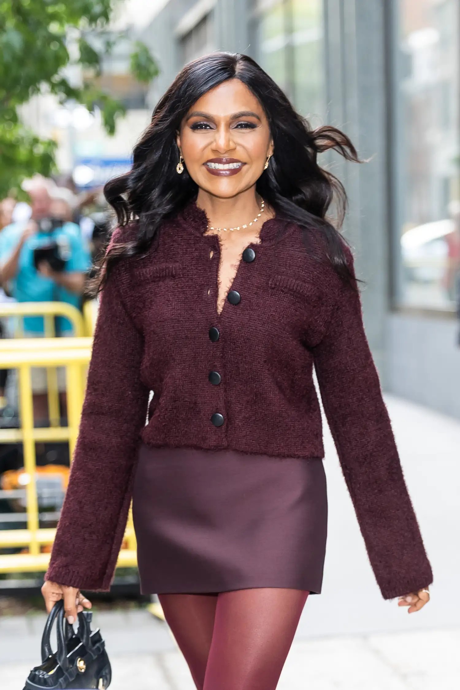 Mindy Kaling wearing a burgundy cardigan and a matching burgundy mini skirt