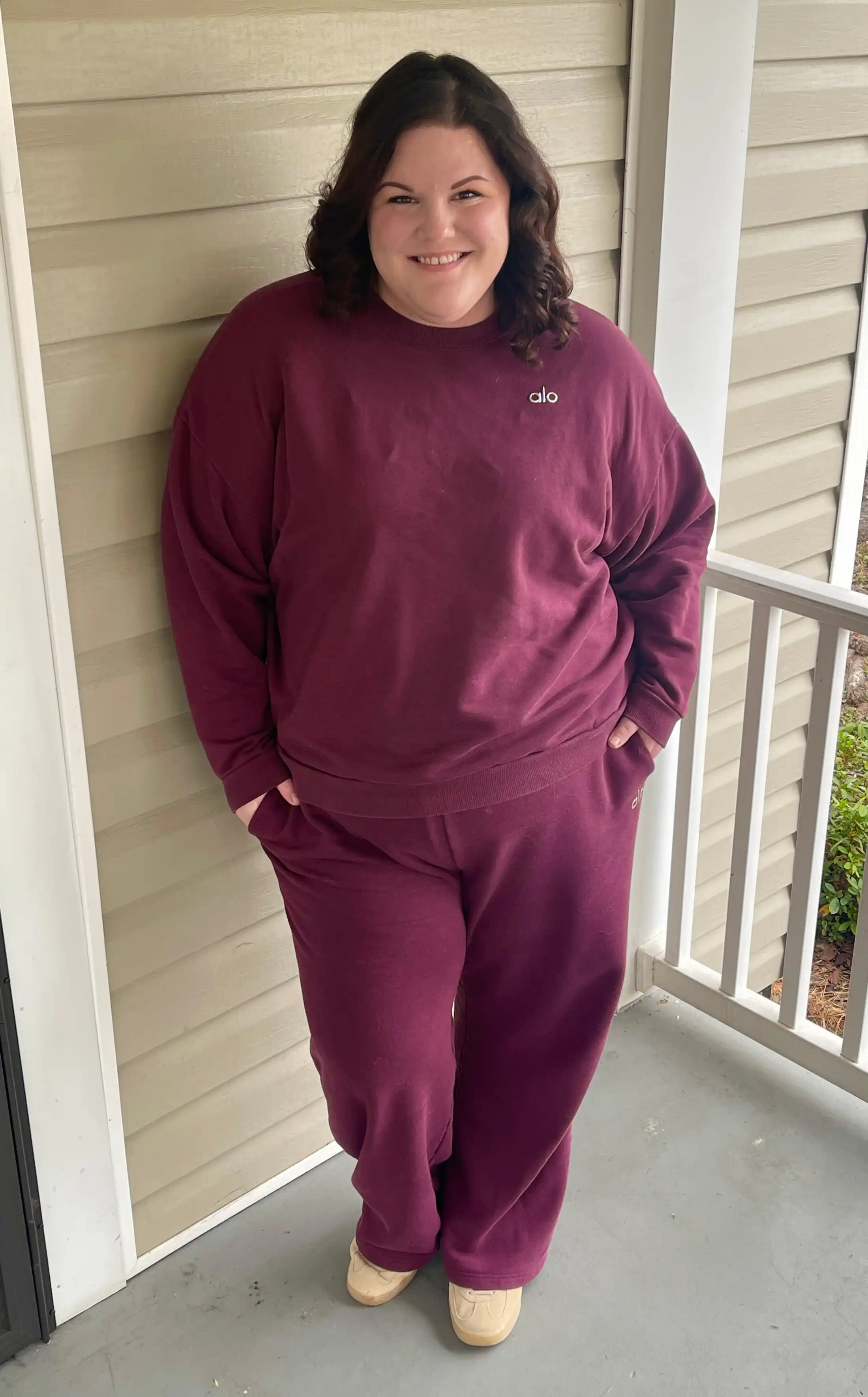A person stands on a porch wearing a loungewear set and smiling at the camera