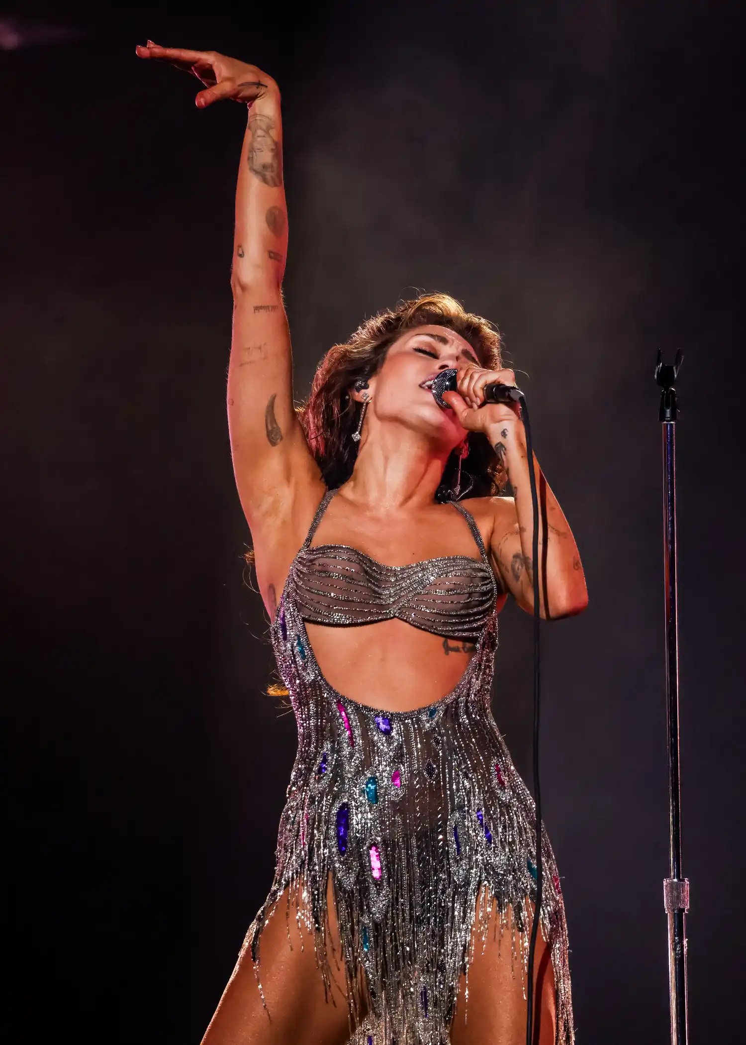 Miley Cyrus wearing a sparkly silver onesie on stage.