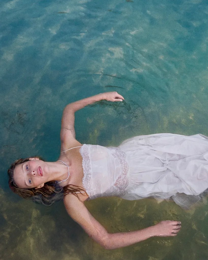 Apple Martin floating in water in a white lace dress.