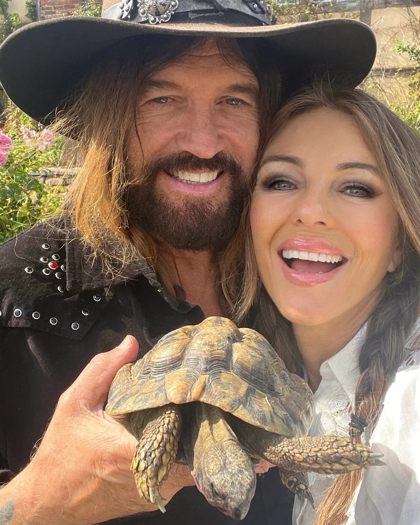 Elizabeth Hurley and Billy Ray Cyrus holding a tortoise.