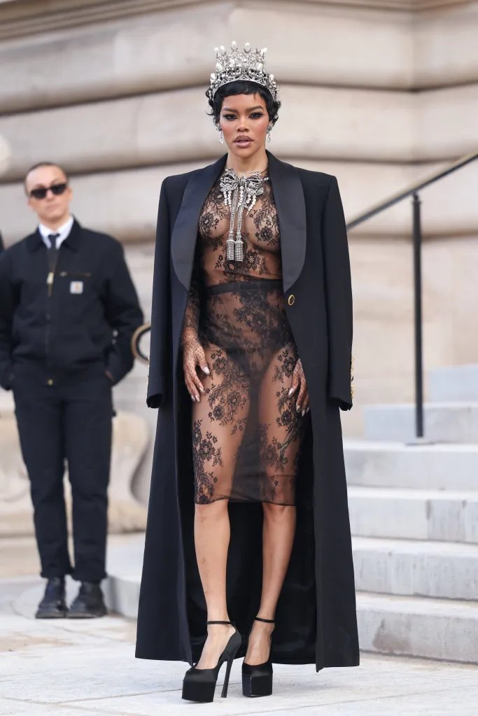 Teyana Taylor wearing a sheer black lace dress, black coat, platform heels, jeweled crown and necklace.