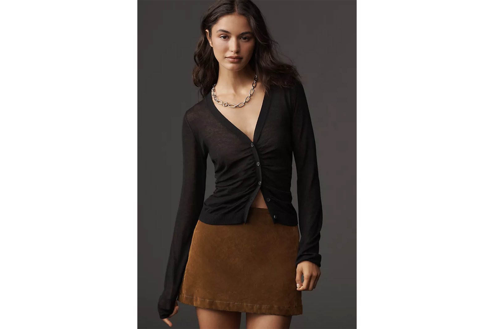 A woman wearing a black long-sleeved sheer cardigan and a brown suede mini skirt.