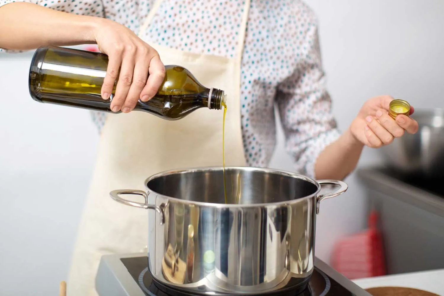 Stock photo of woman adding oil into a pot on the stove
