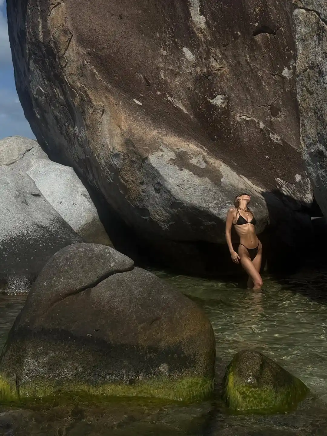 Bella Hadid in a black string bikini in a pool by a huge rock