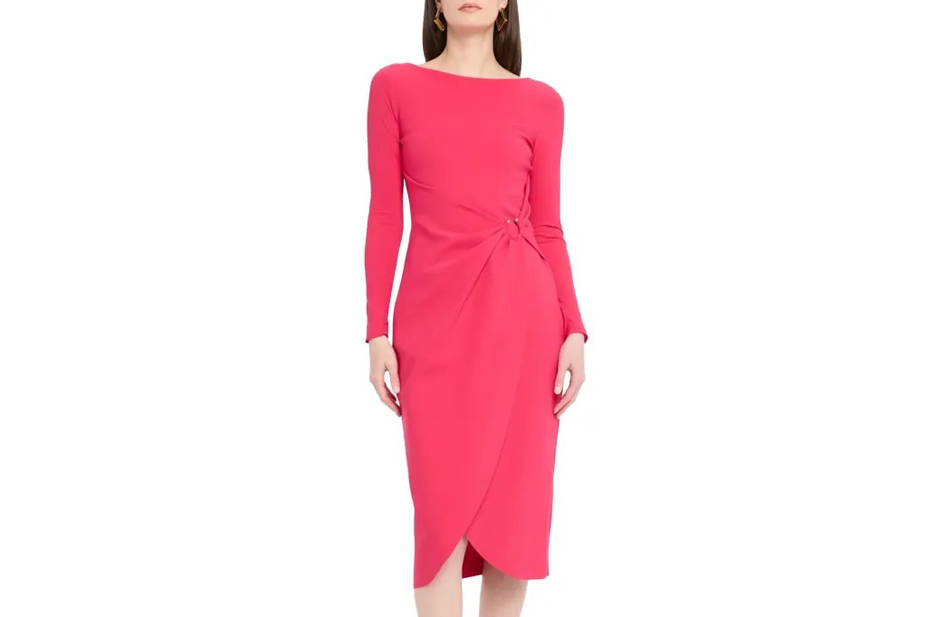 Woman wearing a coral pink long-sleeved boat neck dress with a side knot at the waist and a tulip hem skirt.