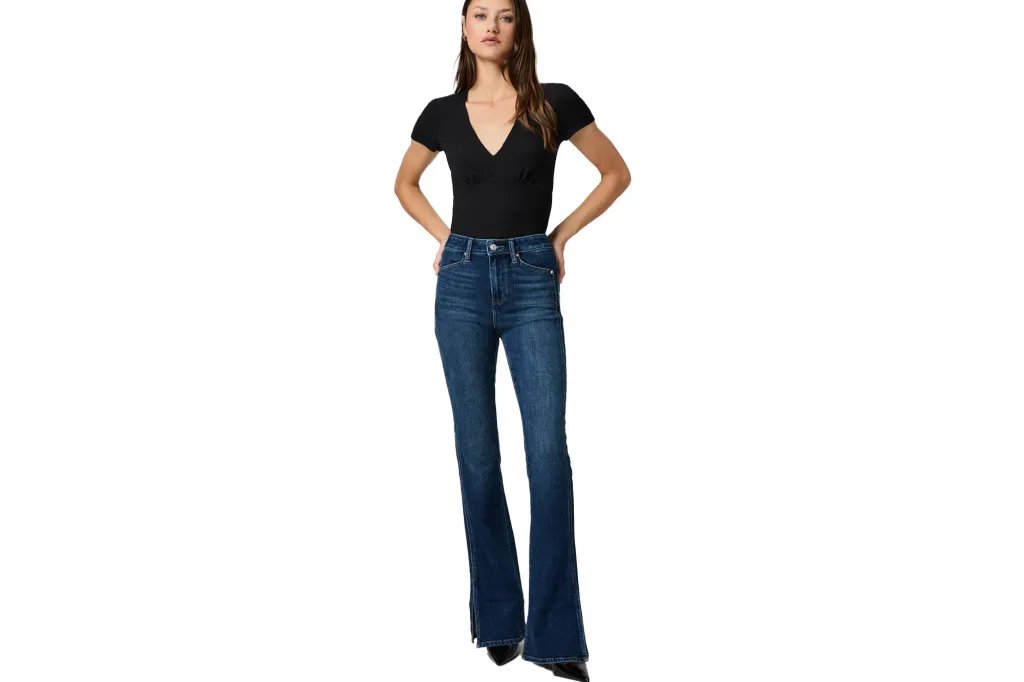 A woman posing in a short-sleeve V-neck shirt and flared jeans with slits.