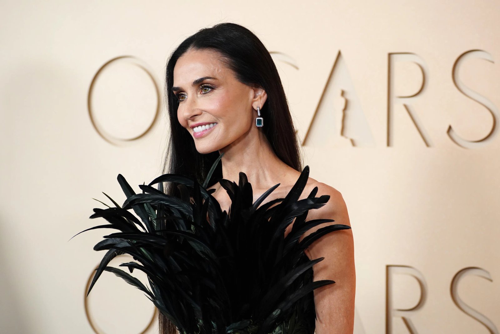Demi Moore on the red carpet in a black feathered dress and emerald earrings.