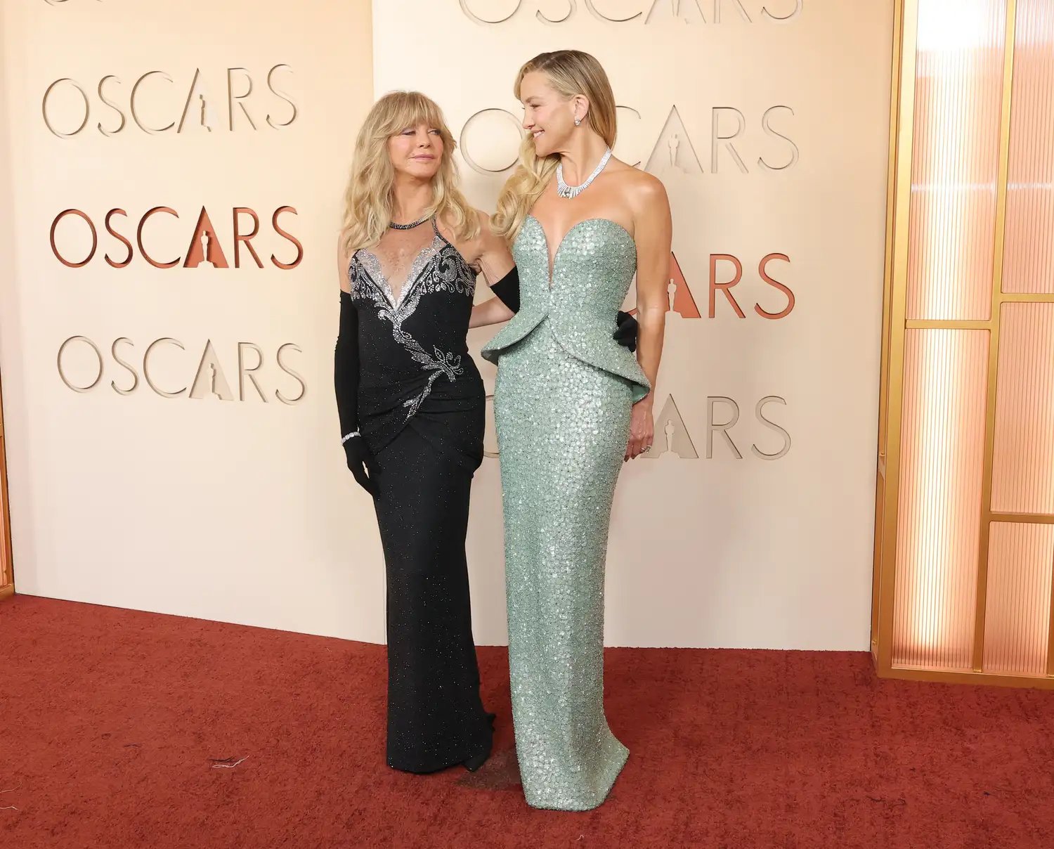 Goldie Hawn with blonde bangs in a black gown on the red carpet at the Oscars 2026 with Kate Hudson in a sparkly mint green peplum gown