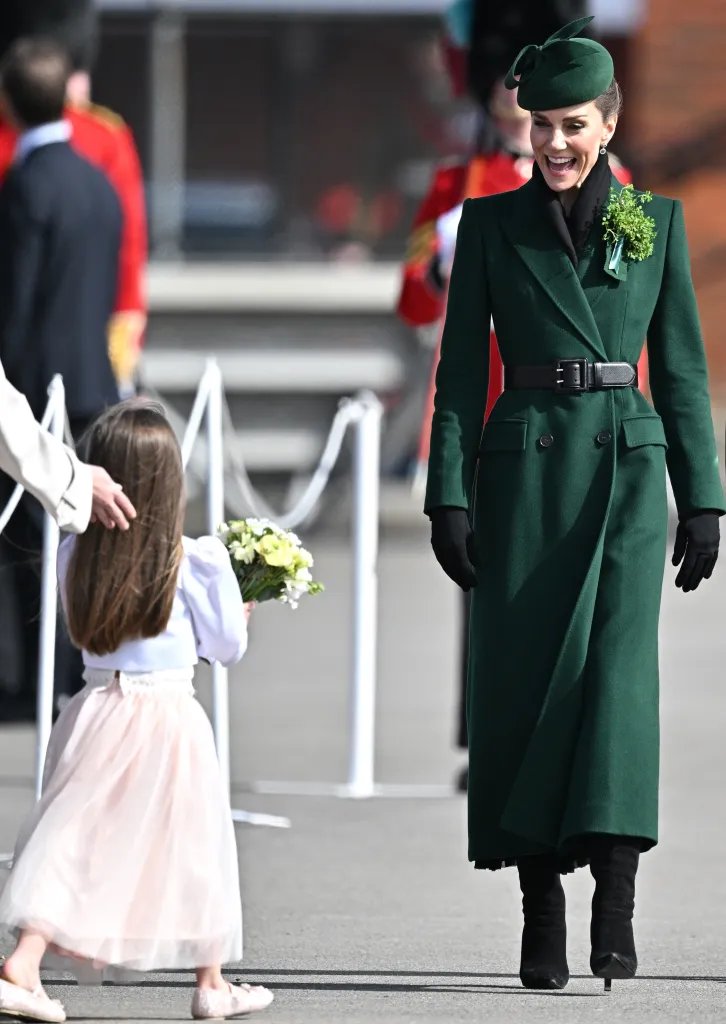 Catherine, Princess of Wales, in a green coat and hat, smiling while receiving flowers from a child.