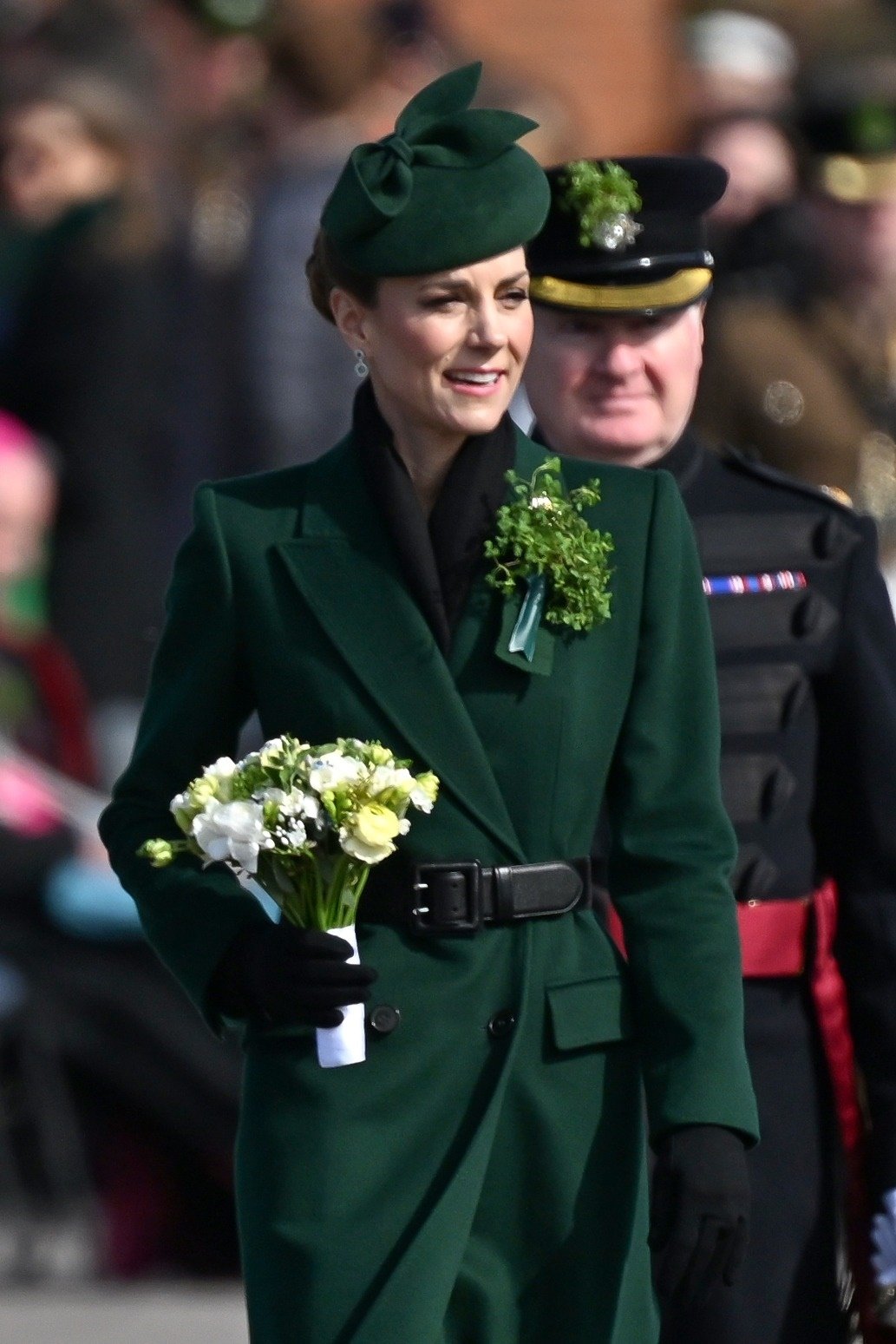 Catherine, Princess of Wales, in a green coat dress, pillbox hat, and black gloves, holding a bouquet, attending The Irish Guards' St Patrick's Day Parade.