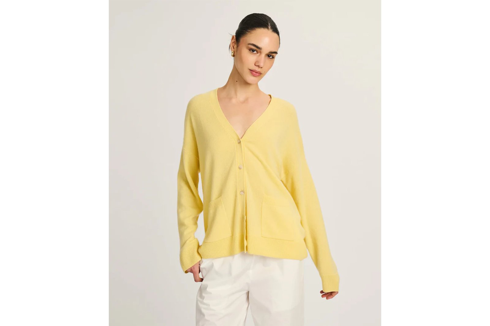 Woman modeling a yellow cardigan with white pants.
