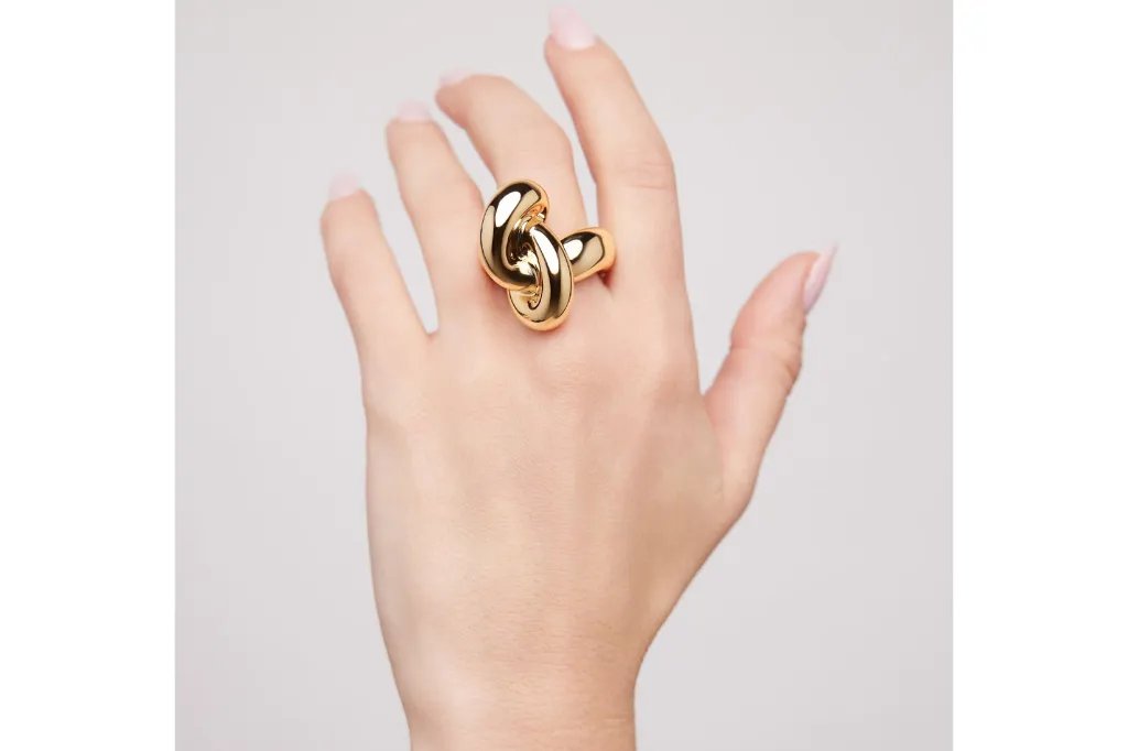 A person's hand wearing a large, shiny gold ring shaped like a knot.