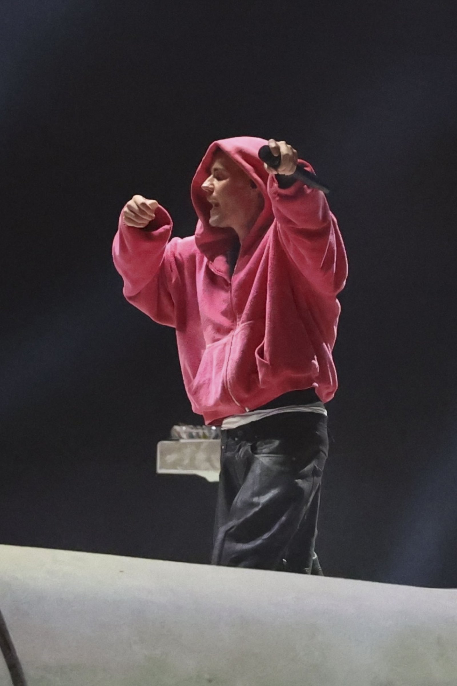 Justin Bieber performing at Coachella in a pink hoodie, holding a microphone.
