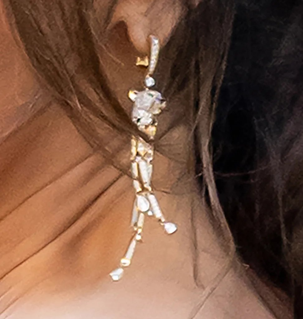 A close-up of a dangling diamond earring on a woman, with her dark hair and neck visible.