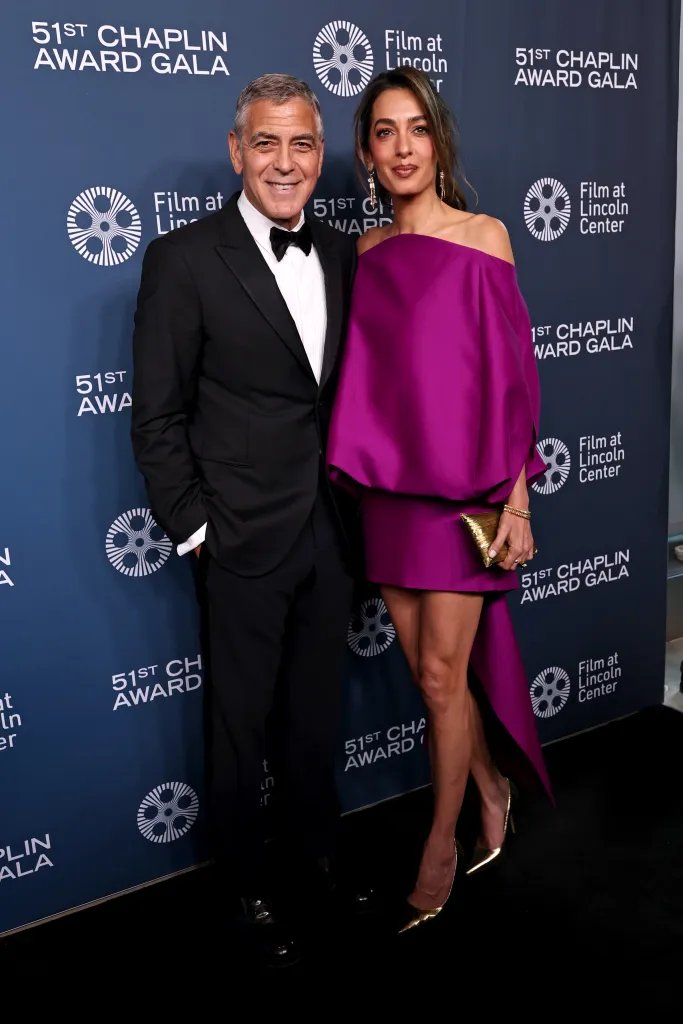 George Clooney in a black tuxedo and Amal Clooney in a magenta dress pose for a photo at the 51st Chaplin Award Gala.