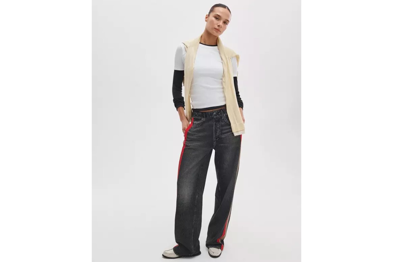 A model wearing Rag & Bone jeans with red stripes, a white t-shirt, and a cream sweater draped over her shoulders.