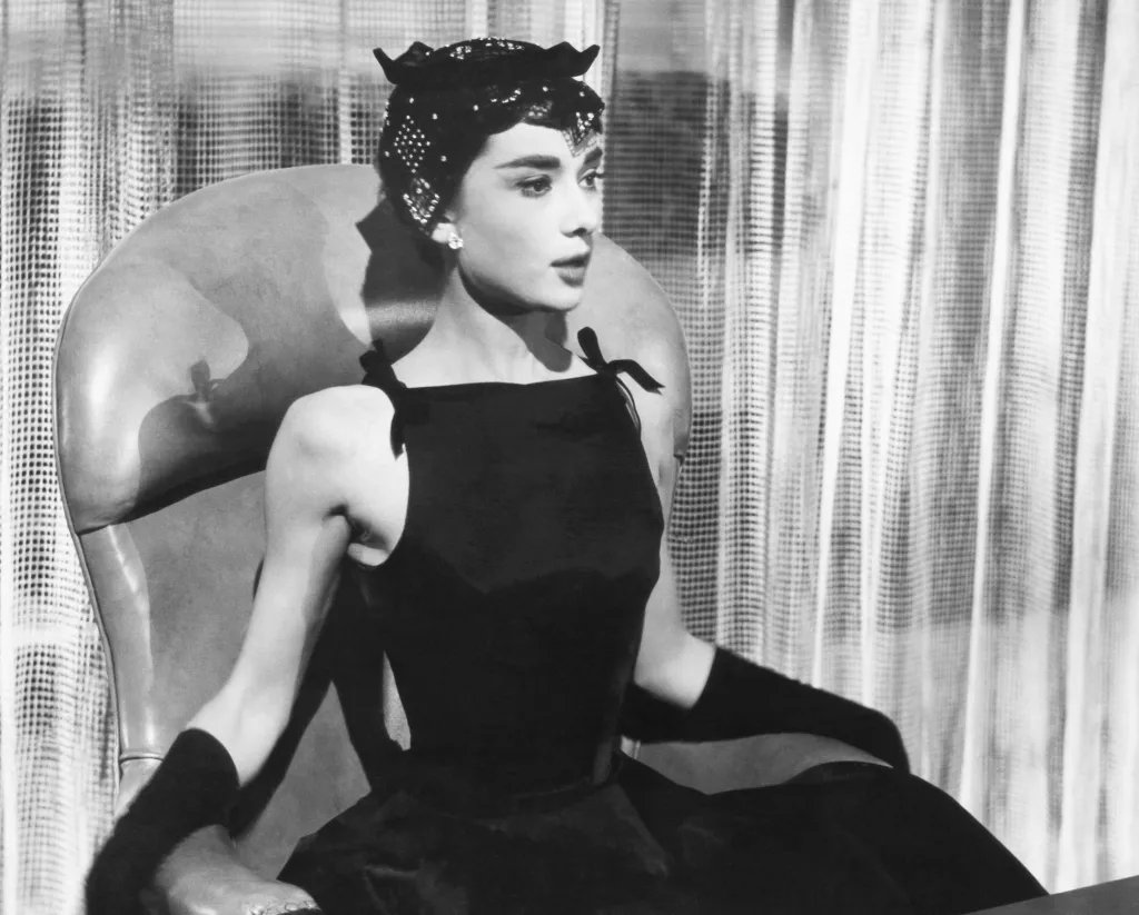 Audrey Hepburn in 'Sabrina' wearing a black dress, long gloves, and a hair accessory.