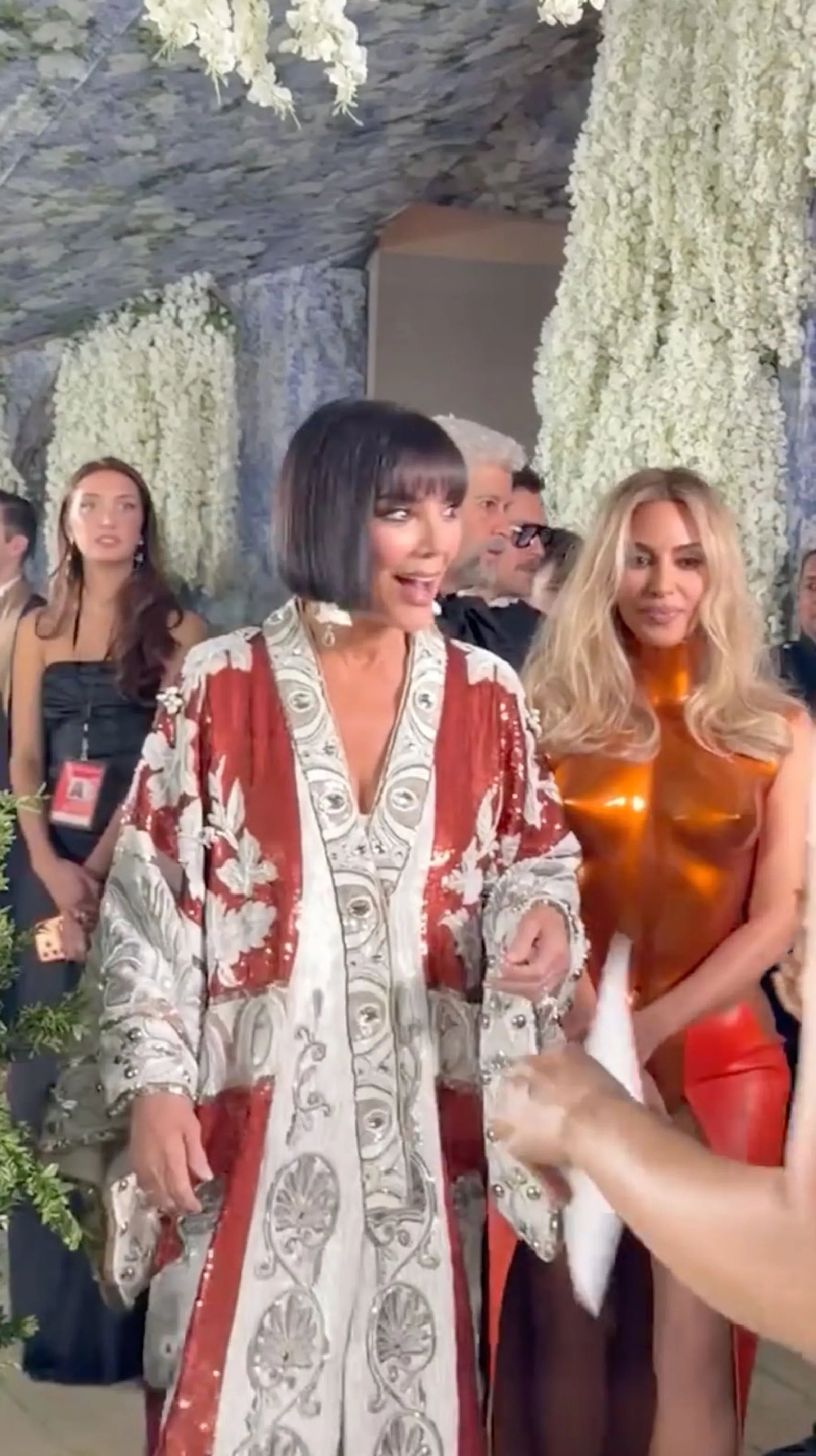 Kris Jenner in a red and white ornate robe-like garment and Kim Kardashian in a copper-colored top and red bottom at the Met Gala.