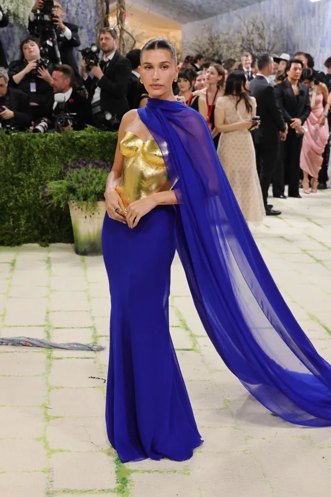 Hailey Bieber in a gold bustier with a royal blue dress and matching cape.