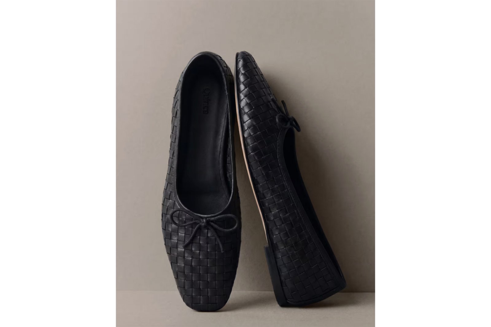 A pair of black woven leather ballet flats with small bows.