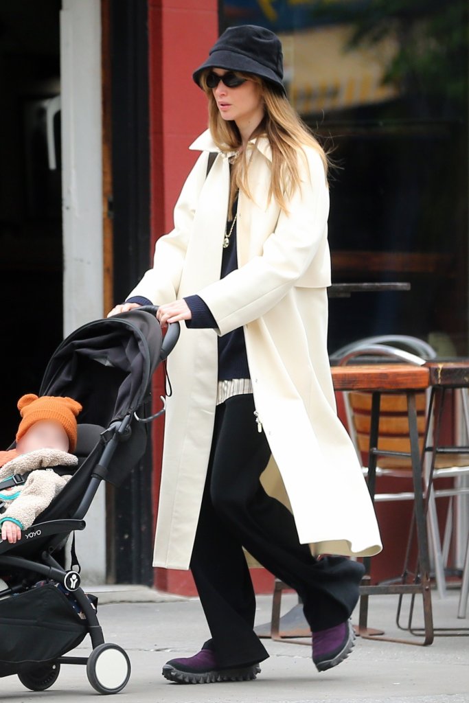 Jennifer Lawrence in a white trench coat and bucket hat pushing a stroller.
