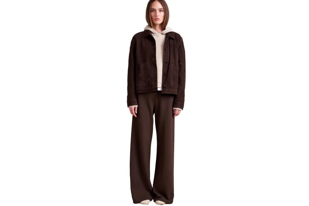 A woman models a brown suede jacket over a cream hoodie, paired with wide-leg brown pants and cream shoes.