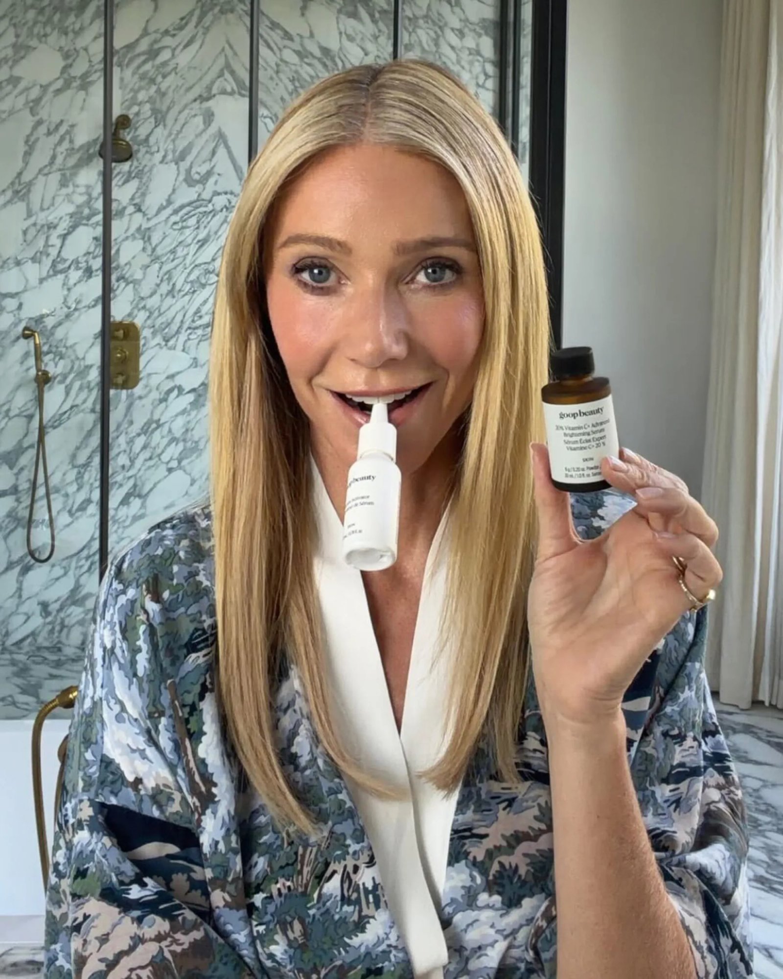 Gwyneth Paltrow holding up two bottles of Goopbeauty Vitamin C Advanced Brightening Serum.